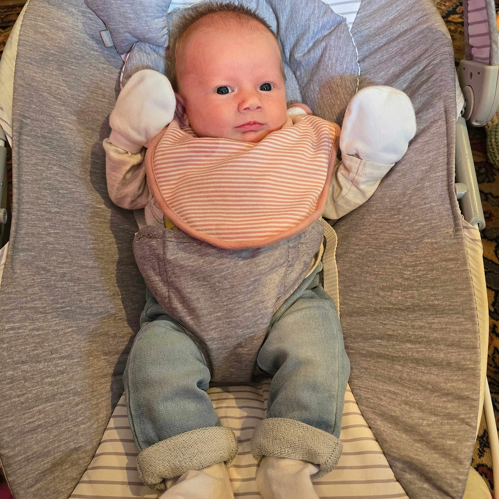 Samantha is registered to the contest to win money with this photo: baby, infant, child, mittens, bib, baby_seat, blue_jeans, white_socks, cozy, cushion, striped, indoor, portrait, cute, young, person, clothing, relaxed, seated, looking