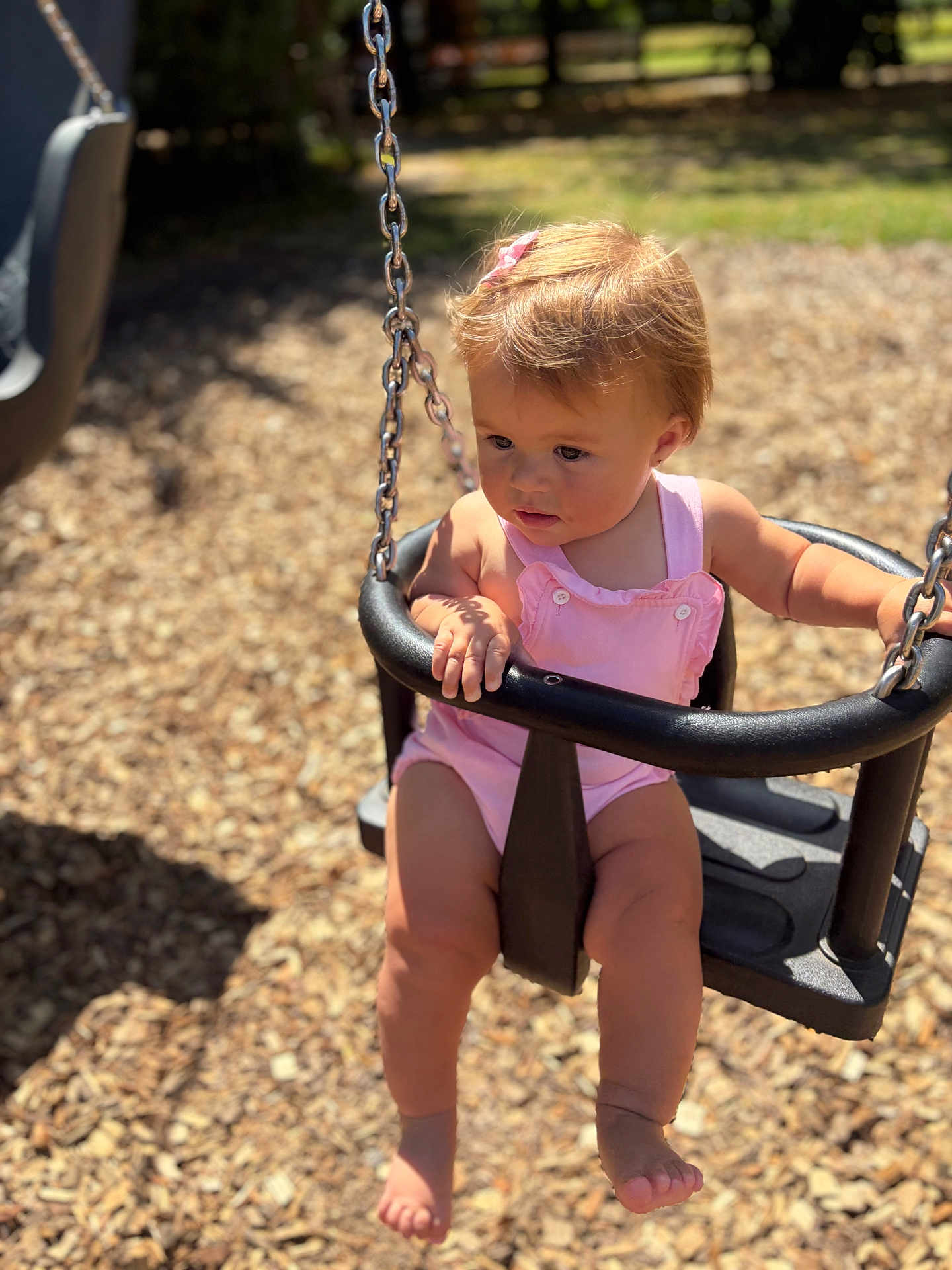Nellie-Jayne is registered to the contest to win money with this photo: toddler, child, swing, playground, outdoor, sunlight, pink_clothing, baby, barefoot, summer, playtime, seat, wood_chips, chain, daylight, person, cute, young_child, safety_bar, nature