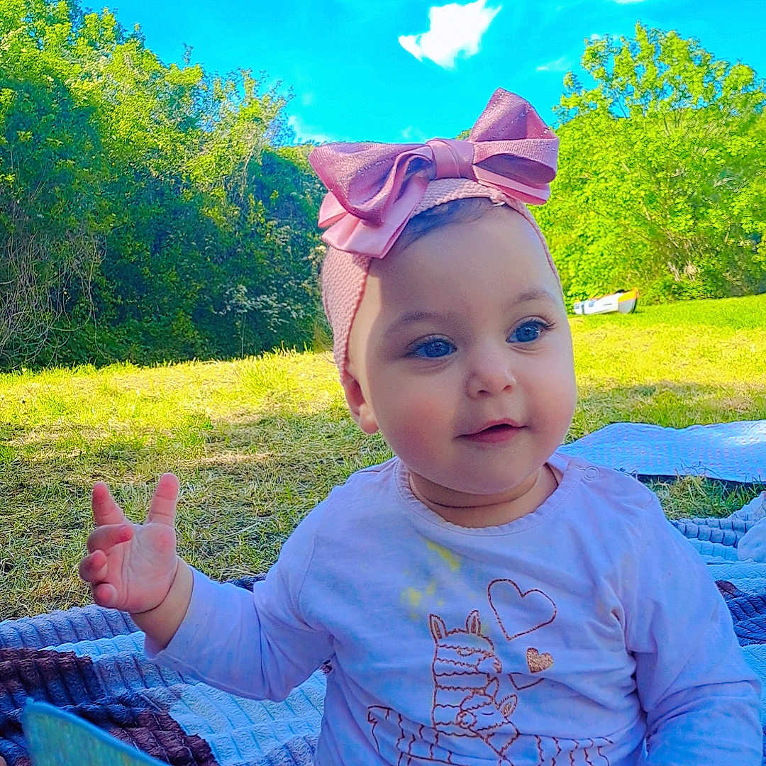 Derine participe au concours pour gagner de l'argent avec cette photo : baby, child, outdoor, blue_sky, greenery, headband, pink_bow, blanket, grass, sunny, cute, smiling, holding, toy, nature, daylight, sitting, happy, infant, playful