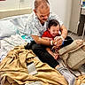 Hamlin is registered to the contest to win money with this photo: baby, child, infant, father, parent, smiling, laughing, cuddling, hospital, hospital_bed, patient, medical_equipment, intravenous_line, blanket, red_shirt, black_pants, handbag, smartphone, indoor, family