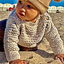 baby, child, knit_sweater, beach, sand, hat, pom_pom, outdoor, sunny, blue_sky, curious, exploring, hands, closeup, portrait, warm_clothing, crawling, playful, person, daylight