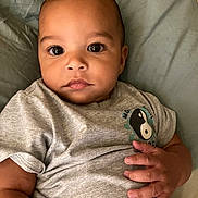 Roman is registered to the contest to win money with this photo: baby, infant, child, face, eyes, hand, skin, tshirt, gray_clothing, lying_down, bed, blanket, portrait, cute, young, indoors, expression, calm, soft_lighting, closeup