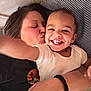toddler, child, woman, smile, kiss, bed, pillow, striped_pillow, white_shirt, black_shirt, affection, happy, family, indoor, closeup, portrait, hand, person, emotion, love