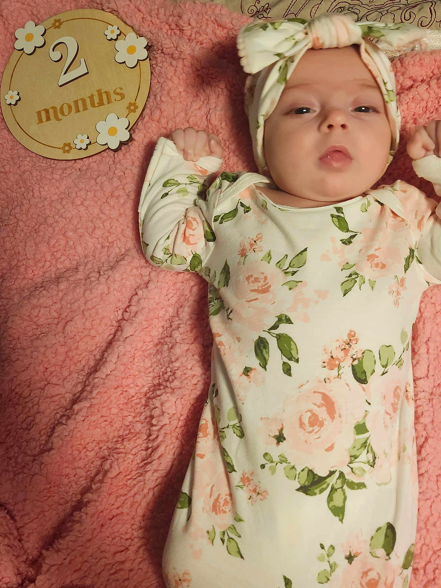 Makayla is registered to the contest to win money with this photo: baby, infant, floral_clothing, headband, pink_blanket, wooden_plaque, milestone, lying_down, cute, newborn, portrait, soft_texture, hand, face, sleepy, child, indoors, celebration, age_marker, cozy