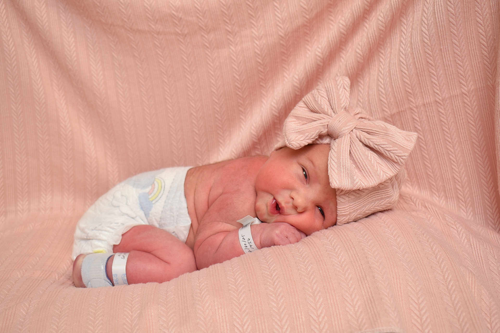 Oliviana is registered to the contest to win money with this photo: baby, newborn, infant, bow_headband, large_bow, diaper, wristband, hospital_band, blanket, pink_blanket, fabric_texture, sleeping, eyes_open, portrait, studio_photo, cute, cozy, soft_lighting, skin, newborn_pose
