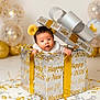 baby, gift_box, new_year, celebration, confetti, balloons, headband, yellow, silver, gold, cute, infant, party, holiday, festive, smiling, face, child, indoors, decorations