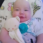 Michael is registered to the contest to win money with this photo: baby, infant, plush_toy, blanket, smile, face, child, cute, soft_toy, person, pattern, flower, bee, cozy, holding, clothing, head, indoors, comfort, young