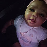 Ro'Miyah joined the competition — help win amazing prizes! baby, infant, child, closeup, portrait, face, head, headband, bow, necklace, onesie, clothing, drool, tongue_out, sitting, dark_background, car_seat, chubby_cheeks, big_eyes, hand