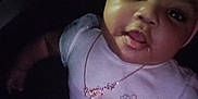 Ro'Miyah is registered to the contest to win money with this photo: baby, infant, child, closeup, portrait, face, head, headband, bow, necklace, onesie, clothing, drool, tongue_out, sitting, dark_background, car_seat, chubby_cheeks, big_eyes, hand