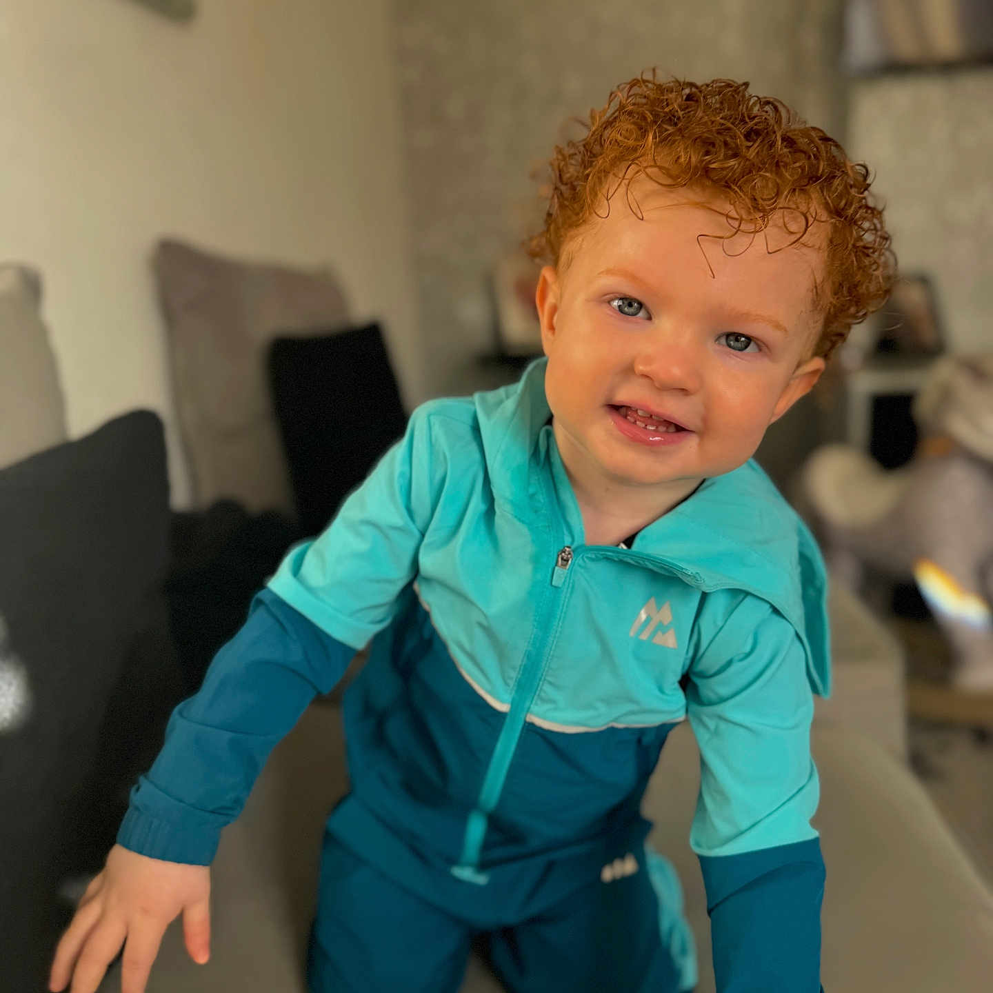 Lkai joined the competition — help win amazing prizes! blue_tracksuit, bright_eyes, casual_clothing, child, couch, cozy, curly_hair, cute, face, hands, happy, indoor, living_room, person, playful, portrait, smiling, toddler, toy, young_child