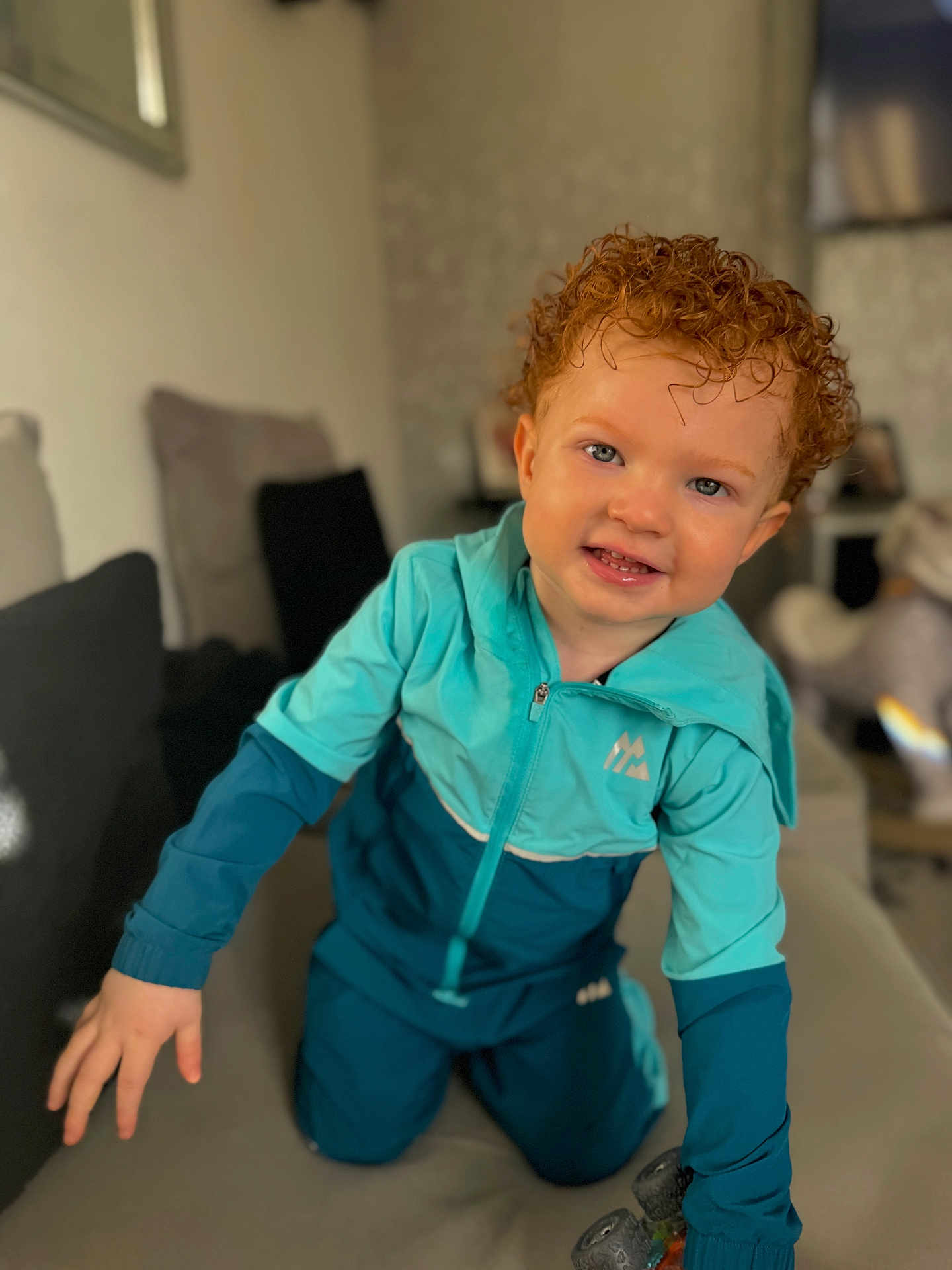 Lkai joined the competition — help win amazing prizes! toddler, child, curly_hair, blue_tracksuit, smiling, indoor, couch, playful, happy, person, young_child, face, hands, toy, living_room, cozy, portrait, casual_clothing, cute, bright_eyes