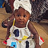 Zunaisha is registered to the contest to win money with this photo: baby, bow, child, colorful, curious, cute, dress, family, floor, foot, footwear, girl, golden_shoes, hand, headband, indoor, person, portrait, sitting, tile
