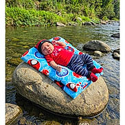 Darvin is registered to the contest to win money with this photo: baby, infant, river, rock, blanket, nature, water, outdoor, greenery, trees, stones, clothing, hat, socks, cute, relaxing, sunlight, peaceful, portrait, child