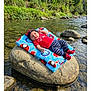 baby, infant, river, rock, blanket, nature, water, outdoor, greenery, trees, stones, clothing, hat, socks, cute, relaxing, sunlight, peaceful, portrait, child