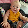 baby, child, infant, smiling, happy, blue_eyes, blonde_hair, stroller, car_seat, sitting, yellow_clothing, romper, barefoot, toes, hand, portrait, indoor, shopping_center, patterned_fabric, safety_harness