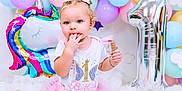 Khloe is registered to the contest to win money with this photo: baby, balloon, bodypart, bread, clothing, dress, face, finger, food, fun, hand, hat, head, party, people, person, photography, portrait, purple, sitting