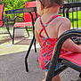 Freyja joined the competition — help win amazing prizes! toddler, child, swimsuit, red, floral_pattern, sandals, outdoor, patio, chair, table, greenery, plant, sunlight, concrete, fence, summer, back_view, baby, person, daytime