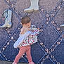 toddler, child, pink_clothing, jacket, leggings, sneakers, boots, wall_display, patterned_background, outdoor, curious, walking, back_view, footwear, pavement, young_child, casual_clothing, baby, exploring, decorative