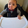 baby, child, high_chair, bow_tie, vest, checkered_shirt, indoor, furniture, table, face, portrait, cute, smile, person, young_child, hands, eyes, expression, clothing, skin