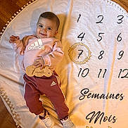 Siana participe au concours pour gagner de l'argent avec cette photo : baby, child, smiling, pink_clothing, adidas, white_shoes, wooden_sign, wooden_wreath, round_blanket, numbers, text, floor, celebration, milestone, indoors, person, happy, portrait, sitting, cute