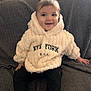 Siana a rejoint le concours — aidez-le/la à gagner de superbes lots ! baby, child, hoodie, smile, sitting, couch, furniture, indoor, person, clothing, happy, face, young, portrait, cozy, text, black_pants, long_sleeves, cute, infant