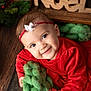 baby, child, christmas, cute, decorations, face, festive, gift, green_blanket, hand, happy, headband, holiday, holiday_season, indoors, knit, portrait, red_dress, smiling, wood_floor