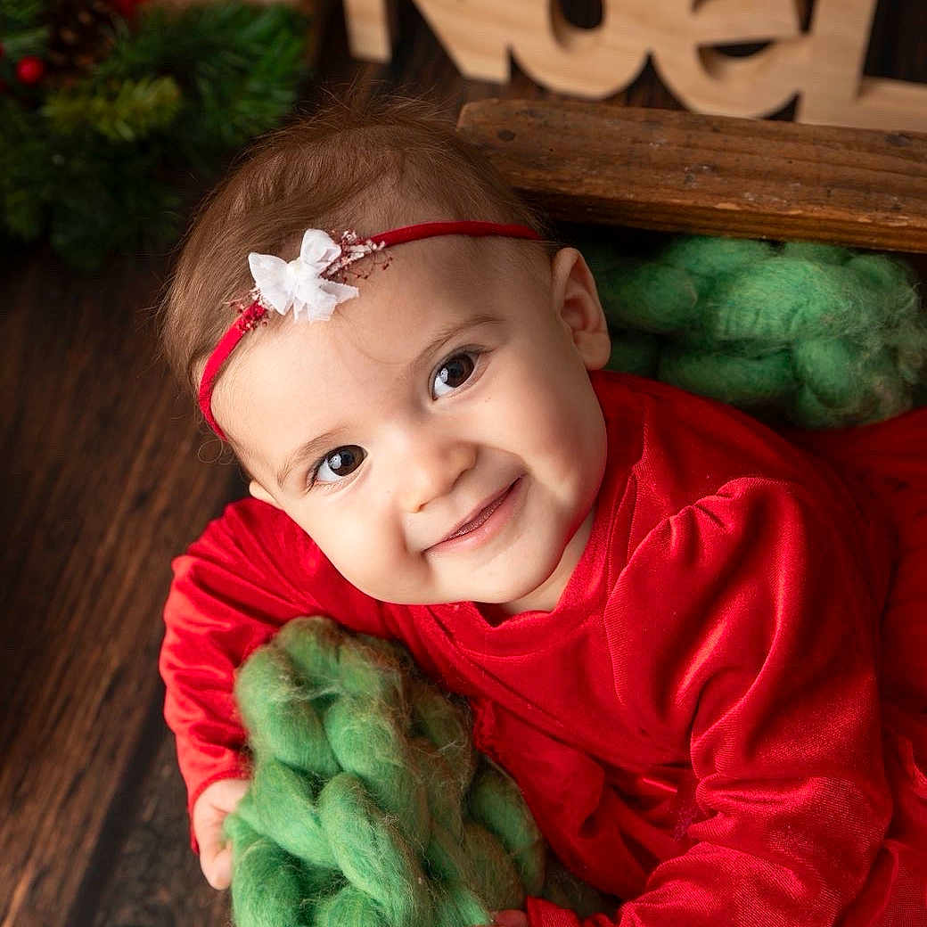 Siana a rejoint le concours — aidez-le/la à gagner de superbes lots ! baby, child, christmas, cute, decorations, face, festive, gift, green_blanket, hand, happy, headband, holiday, holiday_season, indoors, knit, portrait, red_dress, smiling, wood_floor