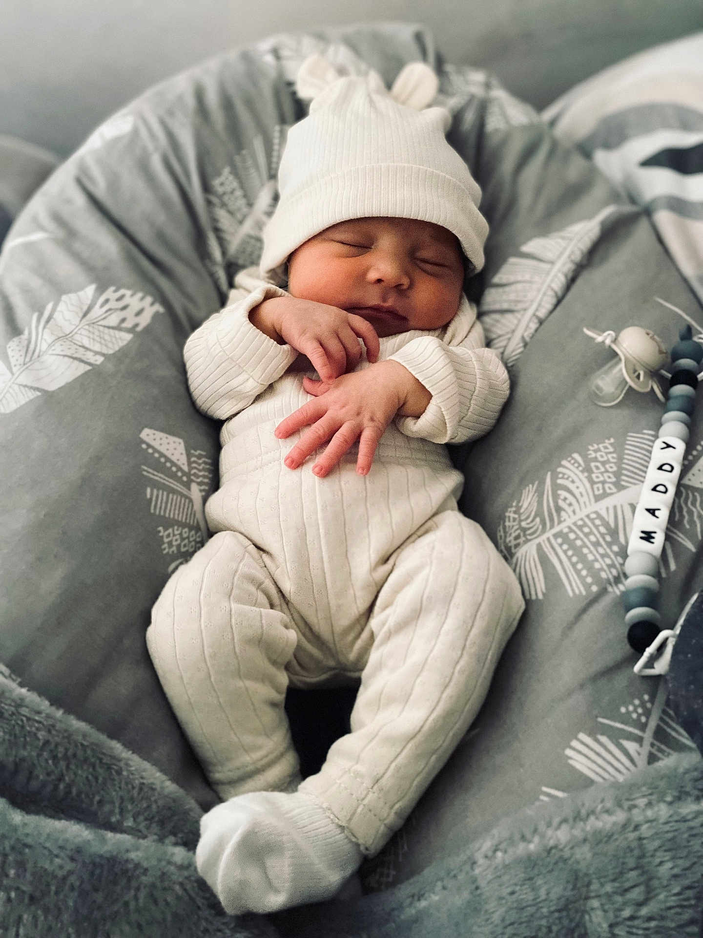 Maddy a rejoint le concours — aidez-le/la à gagner de superbes lots ! baby, sleeping, infant, knitwear, hat, white_clothing, pacifier, cushion, soft_texture, gray_background, hand_position, cozy, newborn, cute, indoor, portrait, peaceful, resting, child, closeup
