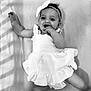 baby, child, infant, dress, headband, bow, smile, happy, hand, fingers, lying_down, soft_surface, monochrome, black_and_white, cute, young, portrait, cheerful, shadow, clothing