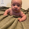 baby, infant, child, portrait, face, curious, indoors, blanket, bed, lying_down, arms, hands, skin, bald, looking_at_camera, home, bedroom, wall, electrical_outlet, cozy