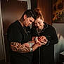 Riya is registered to the contest to win money with this photo: adult, affection, baby, black_clothing, diaper, door, family, happy, holding, indoor, light, love, newborn, parent, person, portrait, room, skin, tattoo, window