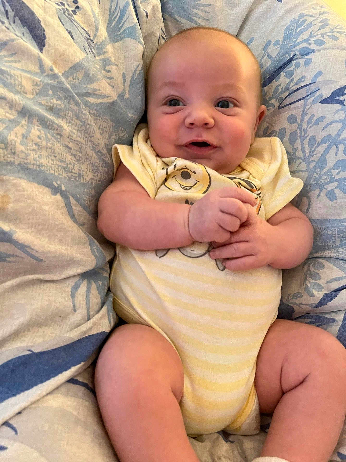 Ezekiel is registered to the contest to win money with this photo: baby, infant, smiling, onesie, yellow_clothing, blanket, blue_pattern, chubby_arms, cute, happy, person, portrait, sitting, indoors, skin, face, head, expression, newborn, comfort