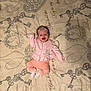 baby, infant, smiling, pink_clothing, bedspread, keys_pattern, script_text, lying_down, raised_arm, white_socks, blonde_hair, cute, indoor, portrait, child, happy, soft_lighting, fabric, cozy, toddler