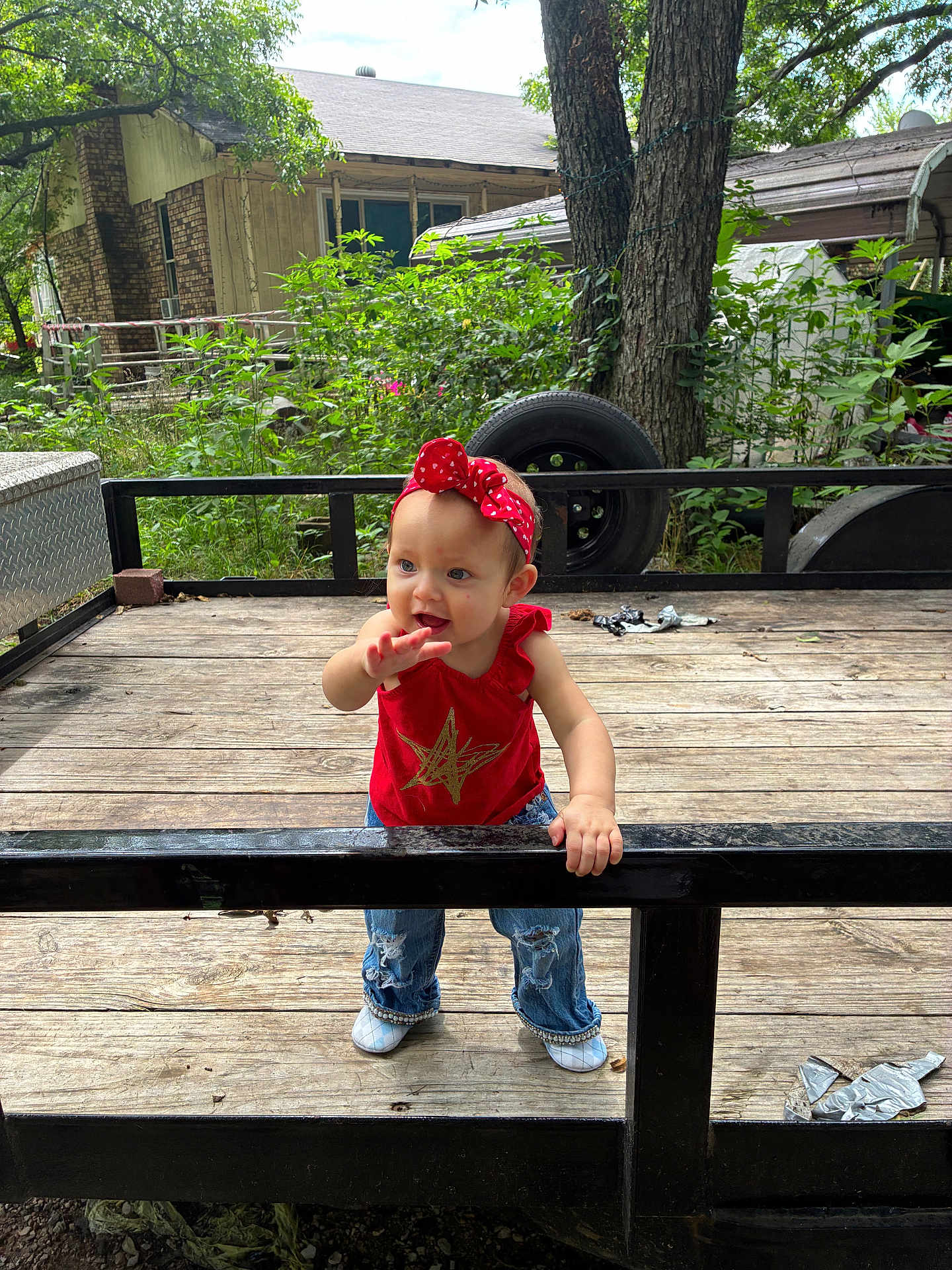 Jo Eva joined the competition — help win amazing prizes! toddler, child, red_headband, red_top, jeans, white_shoes, wooden_deck, black_railing, tree, greenery, tire, rustic_house, outdoor, curious_expression, standing, daylight, casual_clothing, nature, baby, playful