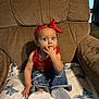 toddler, child, red_headband, red_top, blue_jeans, white_shoes, blanket, stitch_character, armchair, indoor, person, furniture, curious, sitting, baby, cute, clothing, home, expression, hand
