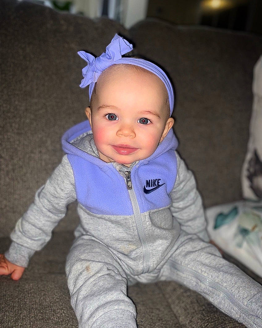 Celine is registered to the contest to win money with this photo: baby, baby_toddler_clothing, cheek, child, comfort, costume_hat, electric_blue, eye, fashion_accessory, fun, grass, happy, headgear, human_body, iris, joy, person, purple, sitting, sleeve