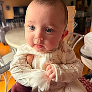 Michael is registered to the contest to win money with this photo: baby, infant, close_up, face, eyes, hands, cozy_clothing, indoor, furniture, table, chair, soft_light, curious_expression, person, portrait, child, holding, warm_tones, cute, newborn