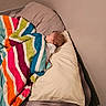 baby, sleeping, bed, blanket, pillow, bedroom, indoors, portrait, child, nap, cozy, colorful, striped_blanket, bedding, peaceful, curly_hair, infant, home, resting, soft_lighting