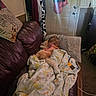 child, toddler, cat, orange_cat, sleeping, cuddling, blanket, quilt, couch, chair, indoor, home, living_room, pet, animal, portrait, cozy, floral, clothing, furniture