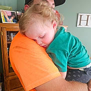 Aryatanner joined the competition — help win amazing prizes! child, toddler, sleeping, adult, parent, 抱抱, portrait, indoor, living_room, orange_shirt, green_shirt, baseball_cap, blond_hair, curly_hair, cuddling, resting, human_pillow, wooden_cabinet, home, family