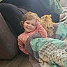 child, toddler, girl, smiling, portrait, dog, pet, blanket, couch, indoors, family, cozy, sitting, playful, salute, long_hair, pink_shirt, home, wood_floor, candid