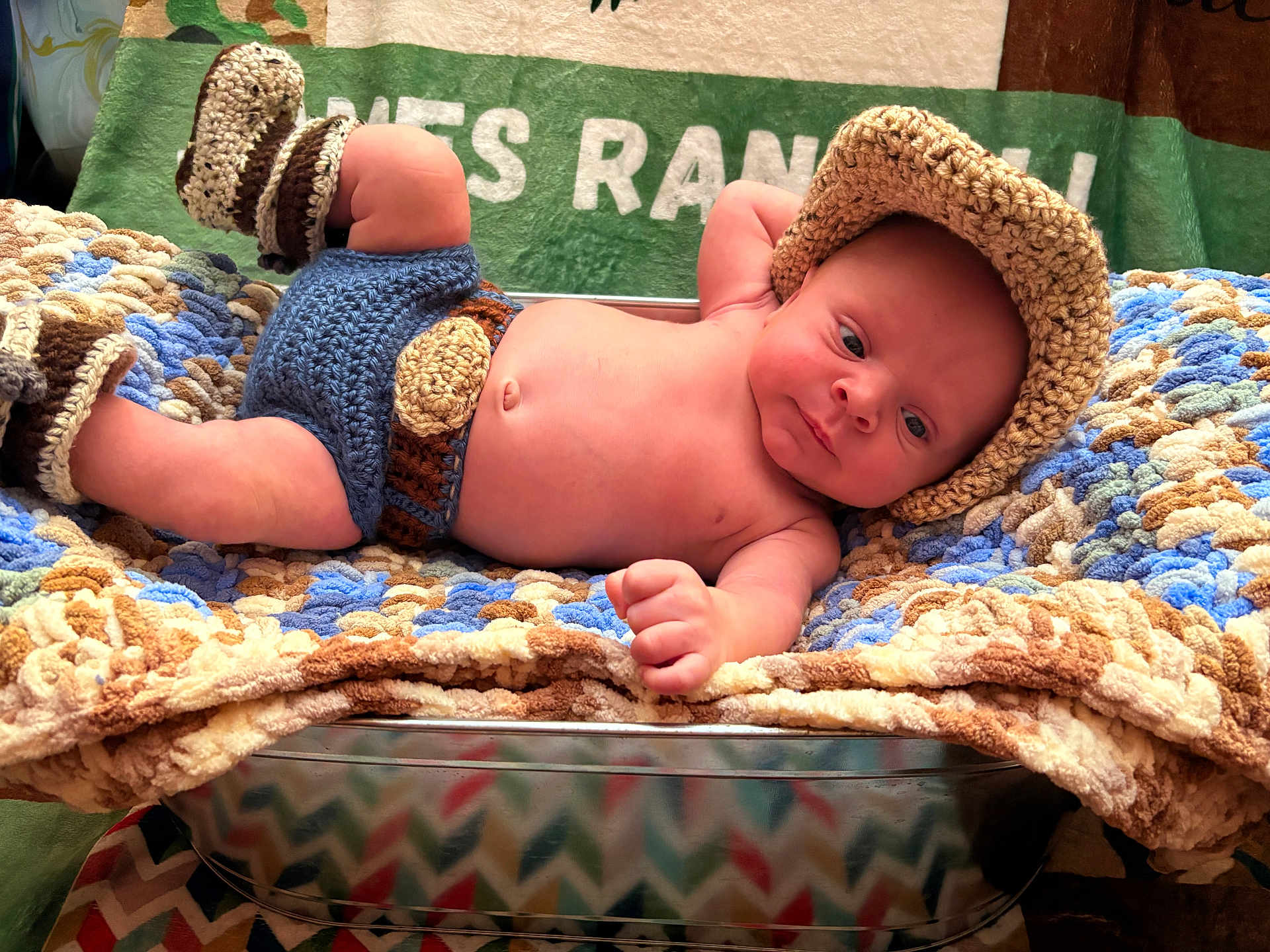James is registered to the contest to win money with this photo: baby, infant, crocheted_blanket, hand_knitted, booties, hat, bare_skin, metal_basket, colorful, cozy, resting, soft_texture, cute, child, portrait, indoor, newborn, relaxed, warm, cute_outfit