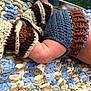 baby, arm, knitted_clothing, blue, brown, blanket, textured, soft, crochet, fabric, closeup, infant, skin, handmade, warm, resting, cozy, colorful, pattern, child