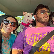 Maya participe au concours pour gagner de l'argent avec cette photo : car_interior, person, dog, smiling, sunglasses, seatbelt, happy, pet, road_trip, sunlight, casual_clothing, short_hair, beard, pink_shirt, blue_shirt, small_dog, large_dog, front_seat, travel, daytime