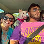 car_interior, person, dog, smiling, sunglasses, seatbelt, happy, pet, road_trip, sunlight, casual_clothing, short_hair, beard, pink_shirt, blue_shirt, small_dog, large_dog, front_seat, travel, daytime