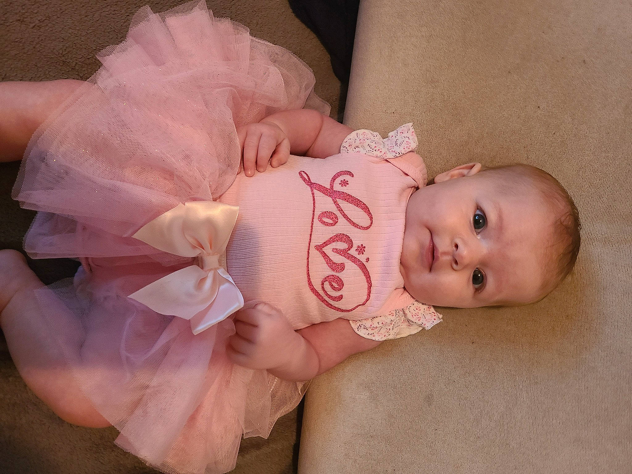 Athena is registered to the contest to win money with this photo: arm, baby, baby_toddler_clothing, cheek, child, comfort, dress, eye, eyelash, face, happy, headgear, headpiece, iris, lip, person, pink, product, skin, sleeve