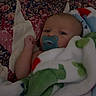 Phoenix is registered to the contest to win money with this photo: baby, infant, child, pacifier, blanket, quilt, bed, lying_down, sleepy, portrait, face, eyes, indoor, cozy, textile, floral_pattern, plush_toy, colorful, home, closeup