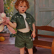 Aliya participe au concours pour gagner de l'argent avec cette photo : child, toddler, curly_hair, plush_toy, green_clothing, shorts, jacket, white_shirt, sneakers, earrings, bench, wooden_furniture, flower_pot, flowers, indoor, portrait, cute, standing, pink_toy, background