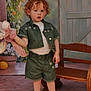 child, toddler, curly_hair, plush_toy, green_clothing, shorts, jacket, white_shirt, sneakers, earrings, bench, wooden_furniture, flower_pot, flowers, indoor, portrait, cute, standing, pink_toy, background
