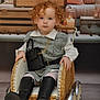 toddler, child, red_hair, curly_hair, wicker_stroller, black_boots, gray_dress, white_shirt, handbag, gold_chain, vintage, wooden_trunks, candles, indoor, portrait, cute, fashion, seated, furniture, decor